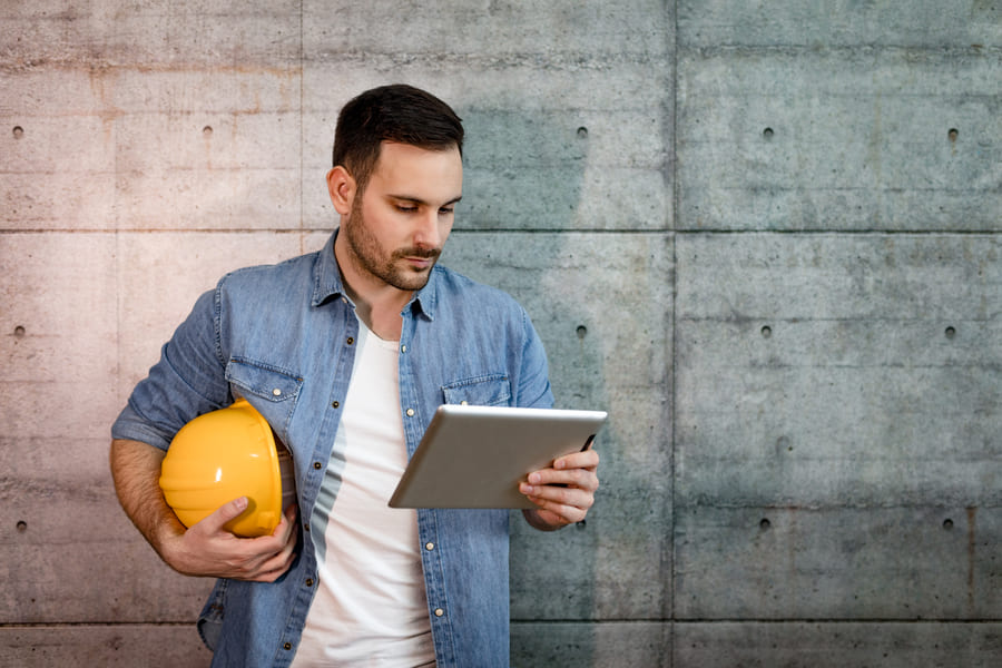 A construction manager holding a yellow hard hat while reviewing project details on a tablet.